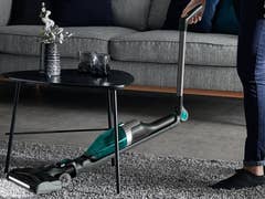 Eine Person benutzt einen Akkusauger von Rowenta unter einem Couchtisch in einem modernen Wohnzimmer.