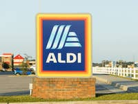 Aldi-Logo auf einem Schild auf einem Parkplatz mit klarem Himmel.