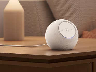 Ein weißer Amazon Echo Dot Max Lautsprecher auf einem Holztisch neben einer Lampe.