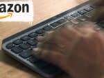 Hände tippen auf einer Logitech MX Keys Mini Tastatur auf einer Holzoberfläche mit einem Amazon-Logo.