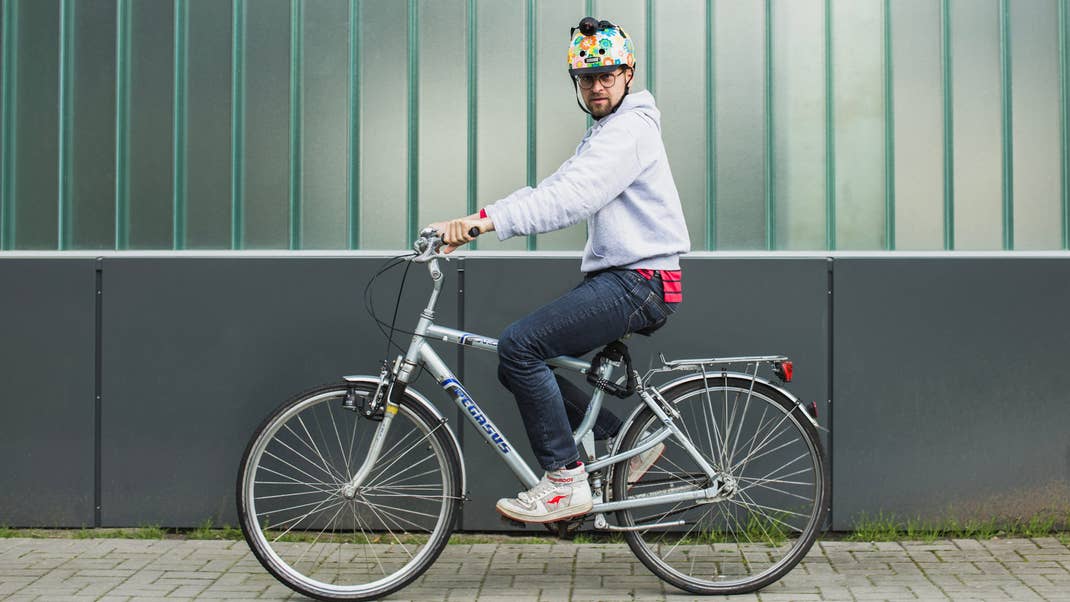 Eine Person mit einem bunten Helm fährt neben einer grünen Wand Fahrrad.