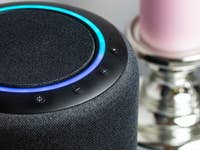Nahaufnahme eines Smart Speakers mit blauer Ringbeleuchtung und Steuerungen, neben einer rosa Kerze.