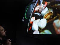 Ein Mann beobachtet ein Nahbild von Meeresfrüchten, das auf einen Bildschirm projiziert wird.