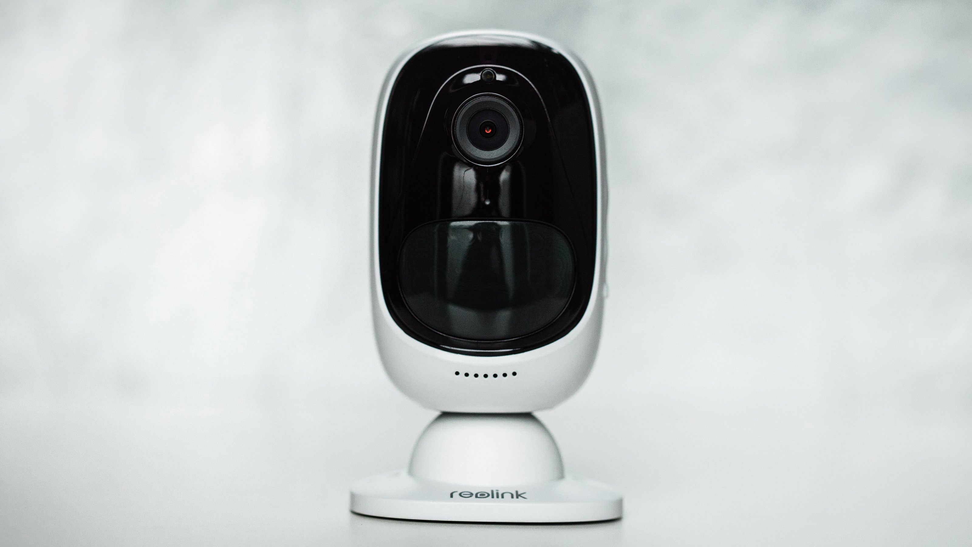 Eine Reolink-Sicherheitskamera auf einer weißen Oberfläche mit verschwommenem Hintergrund.