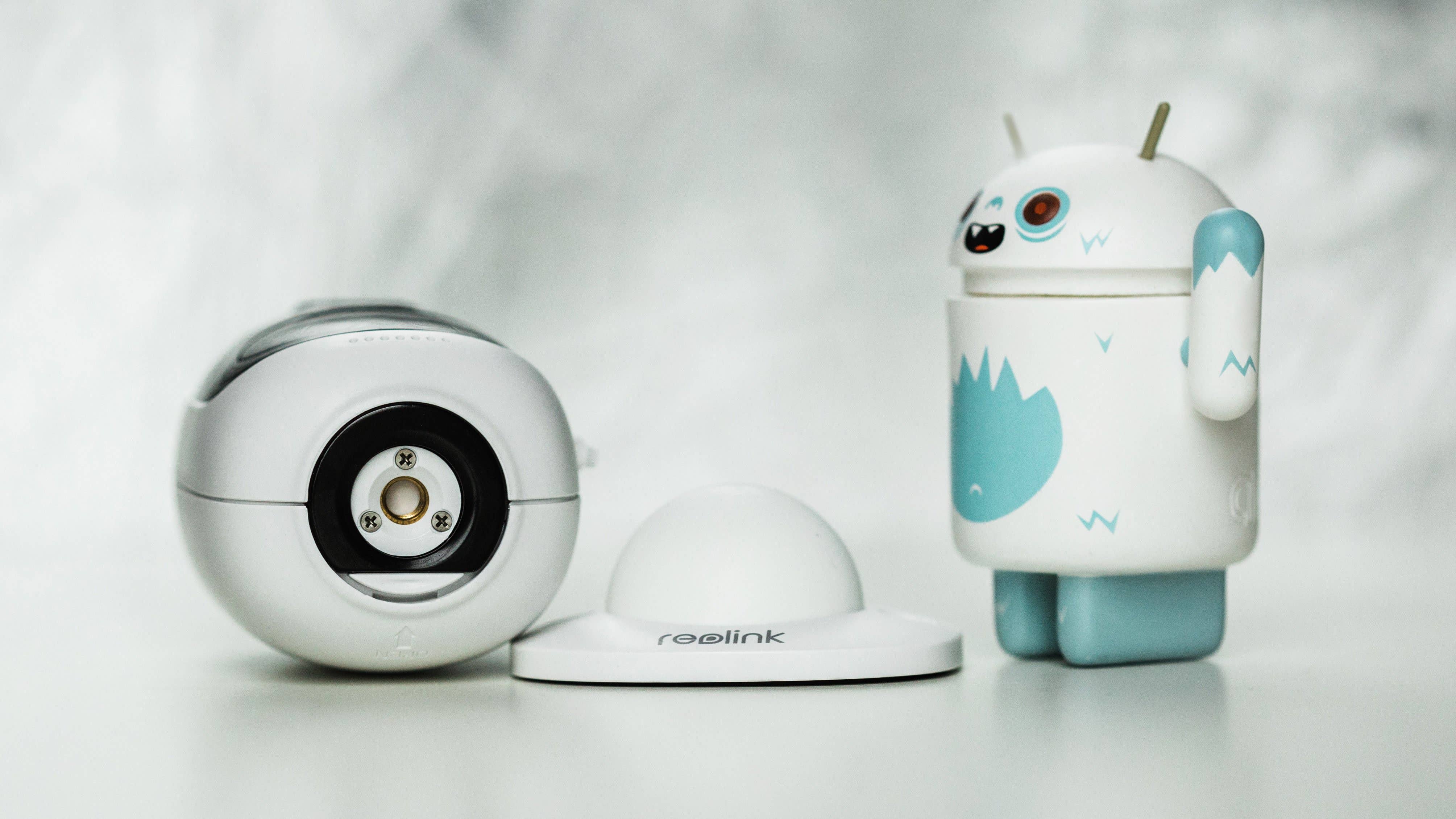 Eine Reolink sicherheitskamera neben einer dekorativen Spielfigur in blau-weißer Gestaltung.