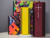 Zwei Ultimate Ears Lautsprecher, einer gelb und einer rot, mit bunten Boxen im Hintergrund.