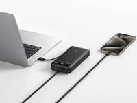 Ein Laptop, der mit einer schwarzen Anker-Powerbank verbunden ist und ein Smartphone auflädt.