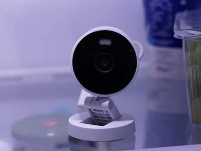 Aqara G100 Smart-Kamera auf einem Regal im Kühlschrank neben einem Behälter mit Trauben.