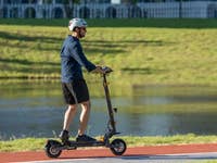 Person fährt einen Ausom L1 EU E-Scooter auf einem Weg am Wasser.