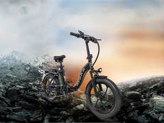 Ein schwarzes Avaka-E-Bike steht auf steinigem Terrain mit Bergen im Hintergrund.