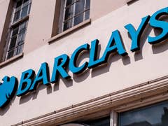 Ein Barclays-Schild mit einem blauen Logo an einer beigen Wand.