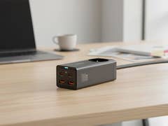 Ein Baseus-Ladegerät mit mehreren USB-Anschlüssen auf einem Holztisch neben einem Laptop und einer Kaffeetasse.