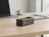 Ein Baseus-Ladegerät mit mehreren USB-Anschlüssen auf einem Holztisch neben einem Laptop und einer Kaffeetasse.