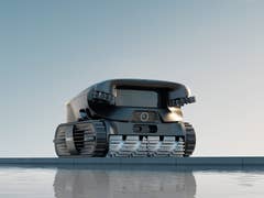 Ein schlanker schwarzer Unterwasserroboter mit kettenähnlichen Raupen, der am Rand des Wassers positioniert ist.