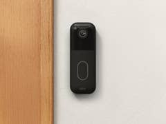 Eine Blink Video-Türklingel, die an einer Wand neben einem Holzrahmen montiert ist.