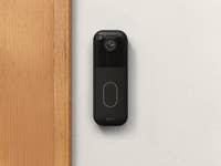 Eine Blink Video-Türklingel, die an einer Wand neben einem Holzrahmen montiert ist.