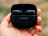 Bose Ultra Open Earbuds in einer Hand, mit leicht geöffnetem Case und sichtbarem Bose-Logo.