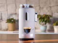 Eine moderne Kaffeemaschine mit einer Tasse Espresso davor und Pflanzen im Hintergrund.