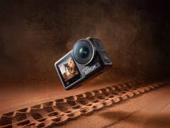 Eine DJI Action 4 Kamera schwebt über einer sandigen Oberfläche mit Reifenabdrücken.