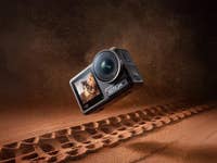 Eine DJI Action 4 Kamera schwebt über einer sandigen Oberfläche mit Reifenabdrücken.