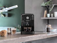 Kaffeevollautomat De'Longhi Magnifica S auf einer Küchenarbeitsplatte mit zwei Tassen Kaffee und einem Gebäck.
