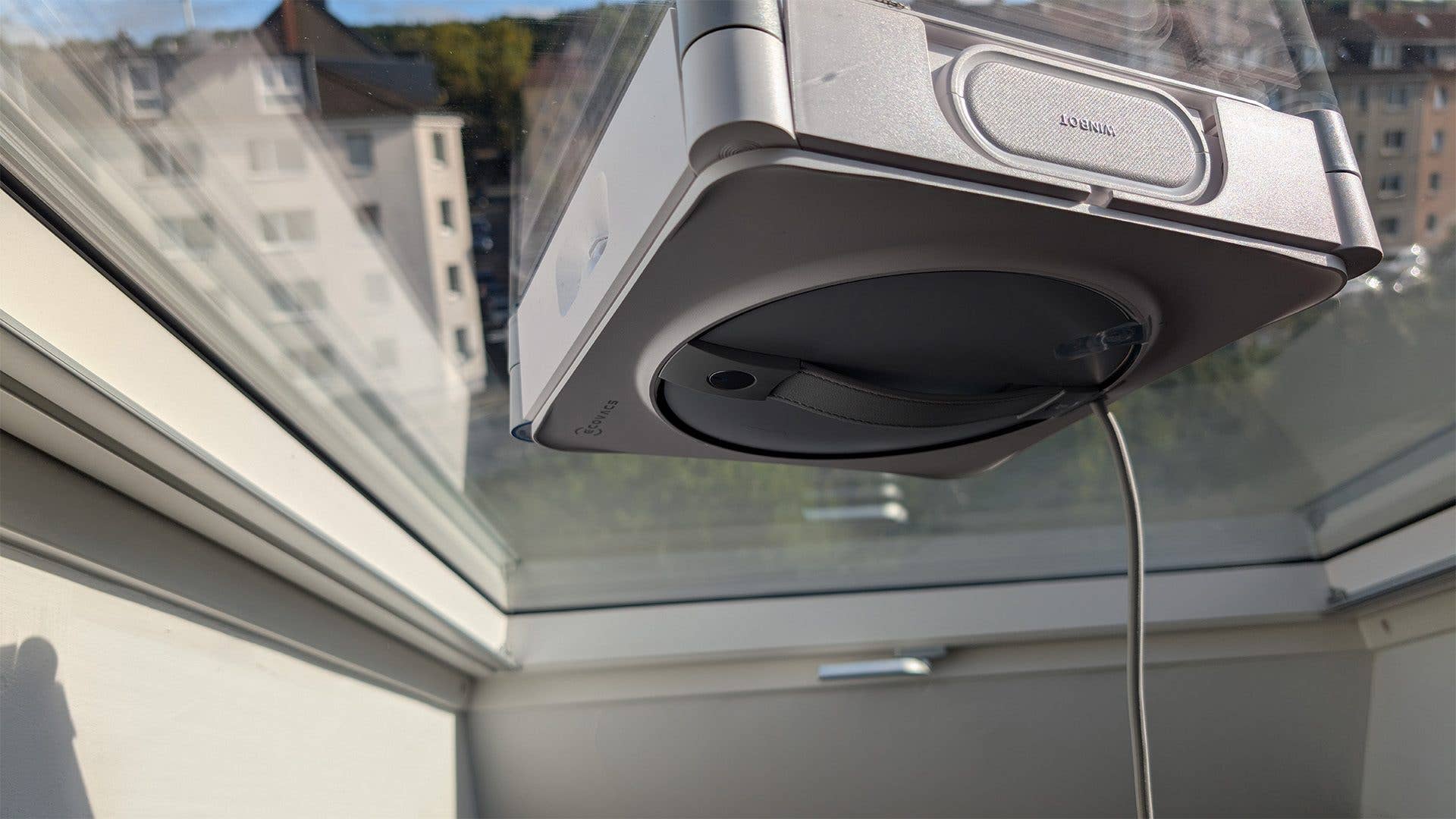 Ein Fensterputzroboter, Ecovacs Winbot W2S Omni, der an einem Fenster befestigt ist.