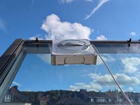 Ein Fensterputzroboter auf einer Glasfläche unter einem blauen Himmel.