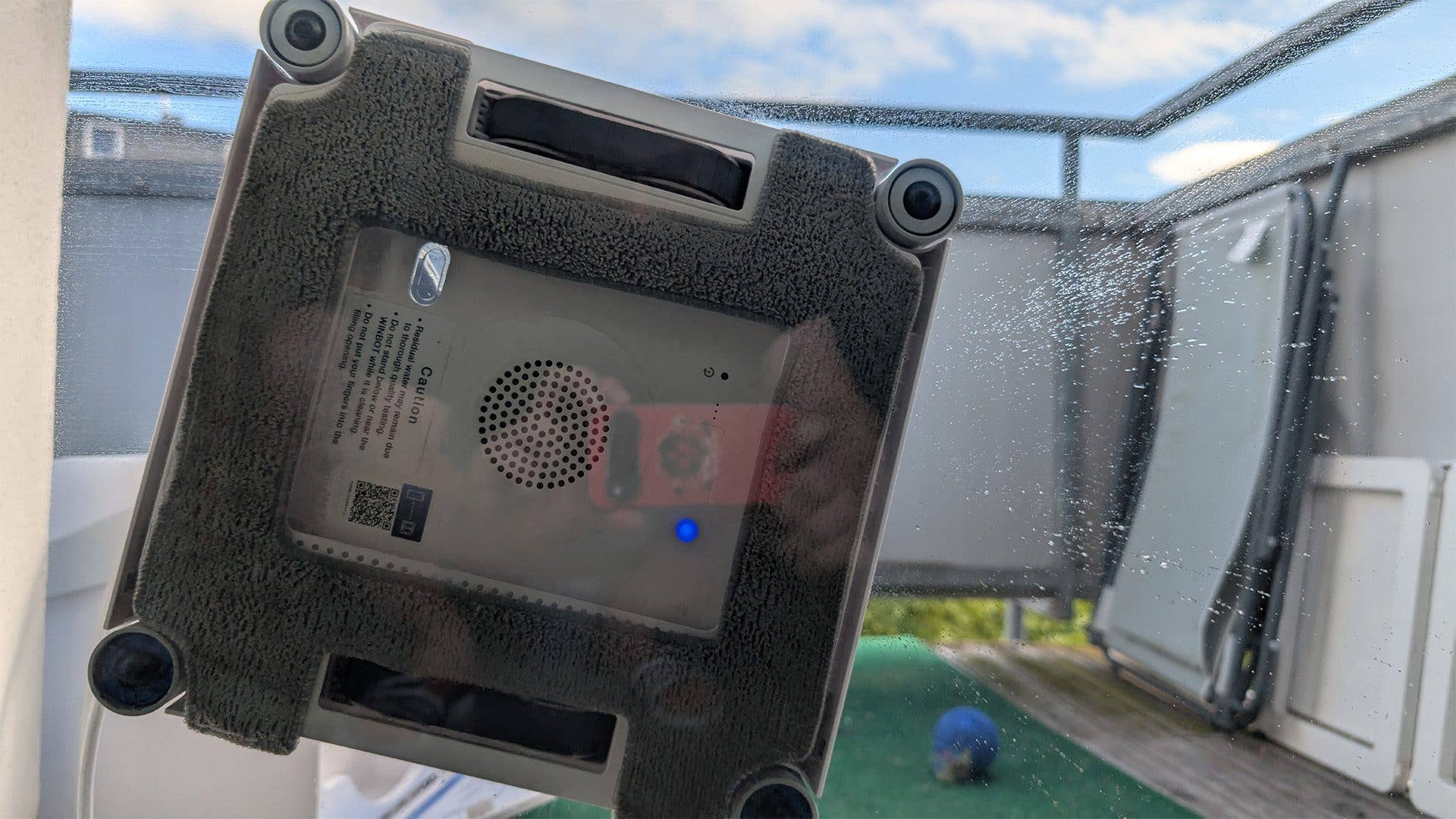 Ein Fensterputzroboter, der an einer Glasoberfläche haftet, mit sichtbarem blauen Anzeigeleuchten.