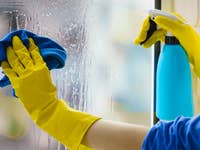 Eine Person putzt ein Fenster mit einem blauen Tuch und einer Sprühflasche.