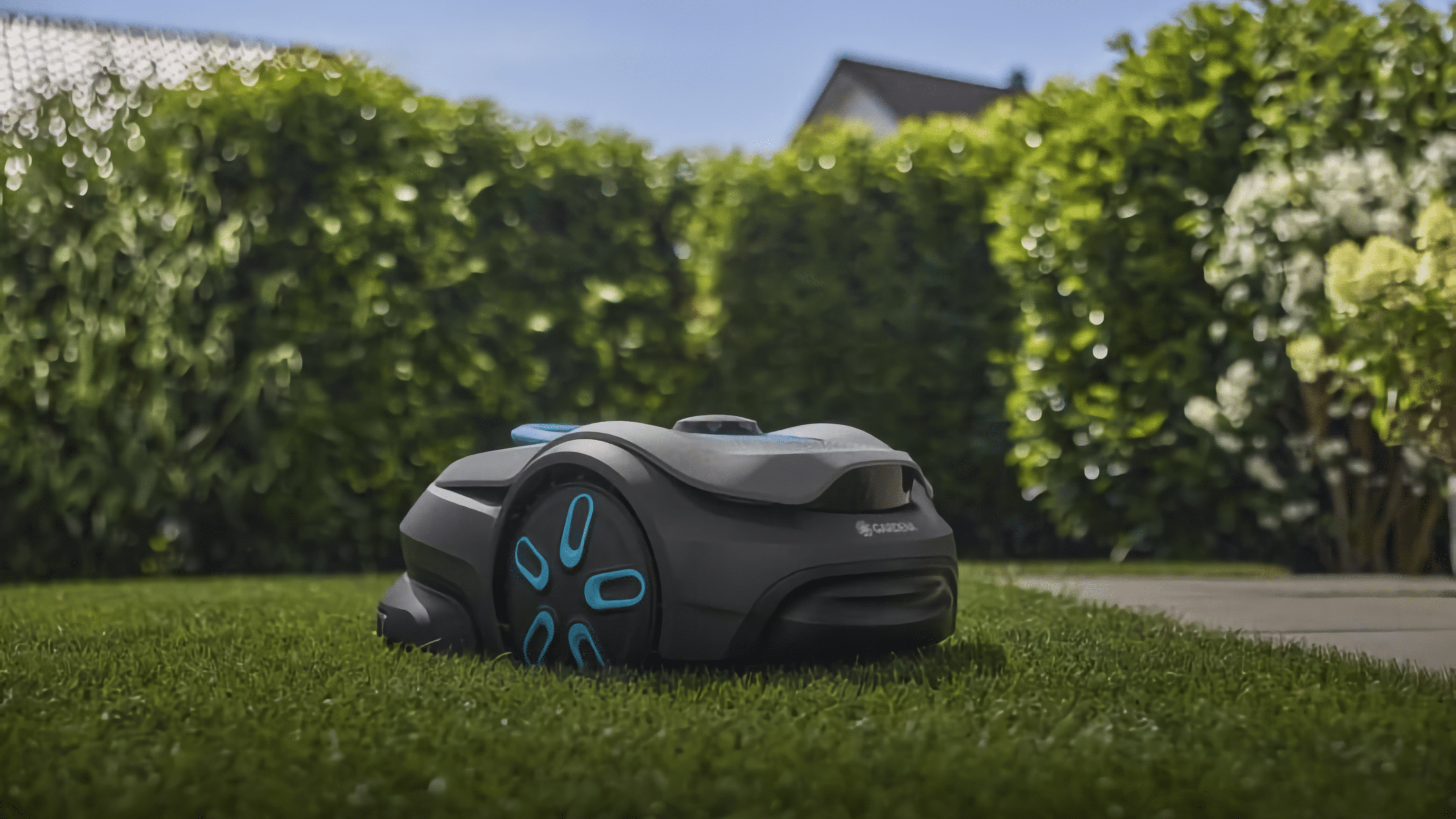 Ein Gardena Smart Sileno Sense Rasenmäher auf grünem Gras neben Hecken.