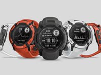 Drei Garmin Instinct 2X Solar-Uhren in Orange, Schwarz und Weiß, die Fitnessmetriken anzeigen.