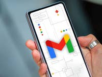 Eine Hand hält ein Smartphone, das das Gmail-Logo auf einem Hintergrund mit geometrischen Formen zeigt.