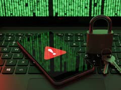 Eine Laptop-Tastatur mit einem Smartphone, das ein Warnsymbol anzeigt, und einem Vorhängeschloss mit Schlüsseln vor grünem Code.
