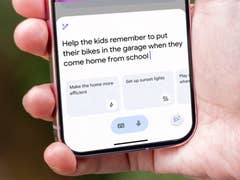 Eine Hand hält ein Smartphone, das eine Erinnerung zeigt: 'Hilf den Kindern, sich daran zu erinnern, ihre Fahrräder in die Garage zu bringen.'
