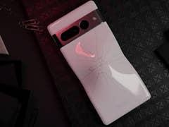 Ein Google Pixel 7 Pro Smartphone mit einem gebrochenen Rücken, das auf einer strukturierten schwarzen Oberfläche mit Büroklammern und Schreibwaren liegt.