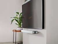 Harman Kardon Citation Multibeam 700 Soundbar unter einem Fernseher mit einer Pflanze in der Nähe.