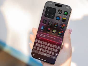 Eine Hand hält ein iPhone, das iOS 18 mit verschiedenen App-Symbolen und einer aktiven Suchleiste zeigt.