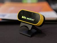 Ein gelbes digitales Device zeigt 'Hello sunshine!' auf einem Tisch an.