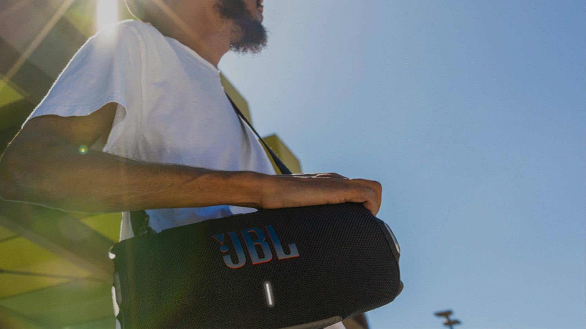 Eine Person in einem weißen T-Shirt hält einen JBL Xtreme 4 tragbaren Lautsprecher. Eine Person in einem weißen T-Shirt hält einen JBL Xtreme 4 tragbaren Lautsprecher.