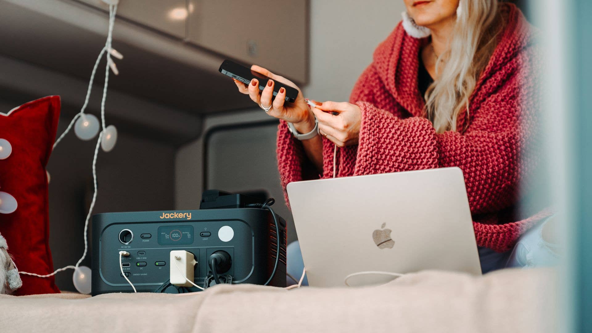 Eine Frau in einer roten Decke benutzt eine Fernbedienung und einen Laptop neben einem Jackery Explorer 500 v2.