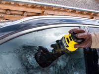 Eine Person verwendet einen Kärcher-Eiskratzer an einem gefrorenen Autofenster.