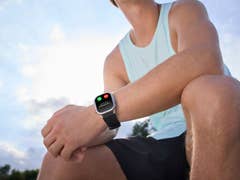 Ein Mann mit einer Kospet P10-Smartwatch, der im Freien sitzt, mit blauem Himmel im Hintergrund.