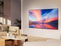 Ein modernes Wohnzimmer mit einem LG OLED77B4 Fernseher, der einen bunten Sonnenuntergang über Wasser zeigt.