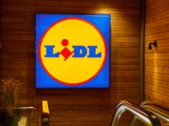 Beleuchtetes Lidl-Logo an einer Holzwand mit angrenzenden Rolltreppen.