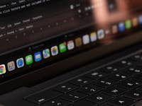 Nahaufnahme eines Laptop-Bildschirms, der das Google Chrome-Symbol im Dock mit Codierungstext im Hintergrund zeigt.