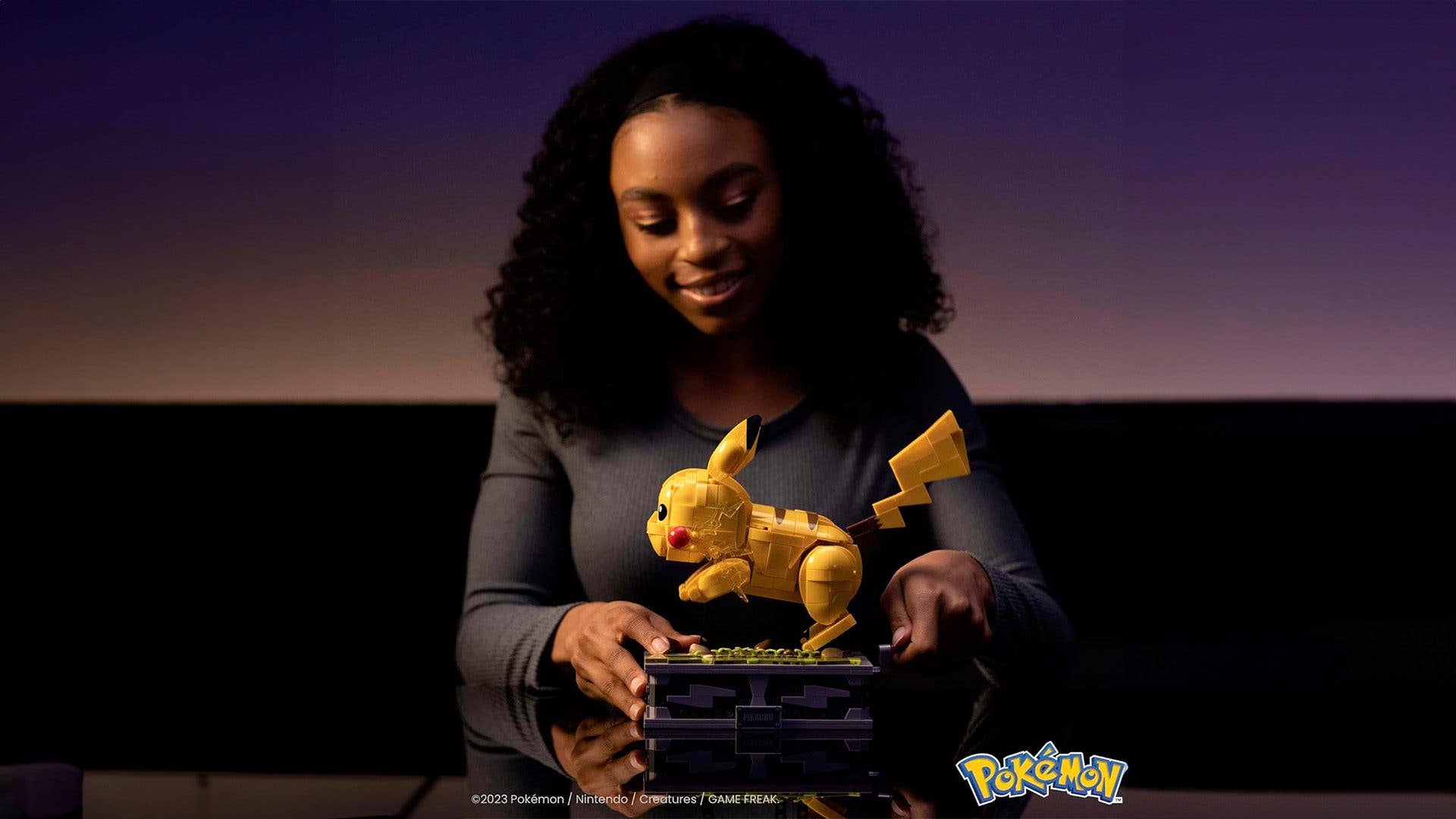 Eine Frau spielt mit einer Pikachu Mega Bloks Figur auf einem Tisch und zeigt Kreativität und Spaß.