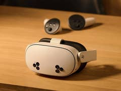 Ein Meta Quest 3S VR-Headset auf einer Holzoberfläche mit zwei Controllern im Hintergrund.