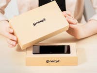 Eine Person packt ein neues Smartphone aus einer NextPit-Box auf einem Tisch aus.