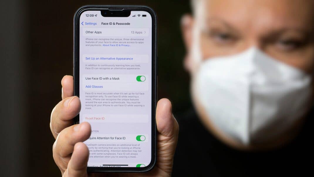 Person mit Maske entsperrt das iPhone 13 mit Face ID. Person mit Maske entsperrt das iPhone 13 mit Face ID.