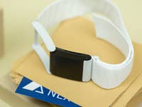 Ein schwarzer Fitness-Tracker mit einem weißen Armband auf einem Stapel Umschläge und einer blauen Karte.